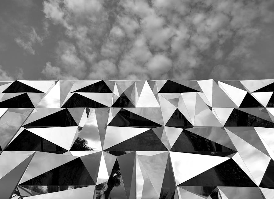 Fotografía en blanco y negro de una moderna fachada geométrica con espejos bajo un cielo nublado.