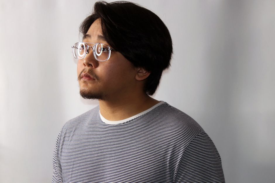 Un hombre pensativo con gafas y una camisa rayada, mirando hacia un lado en un entorno de estudio.