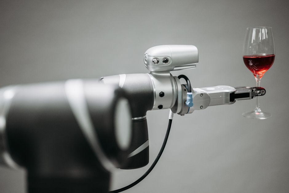 Un brazo robótico sosteniendo cuidadosamente una copa de vino tinto sobre un fondo neutro, mostrando innovación.
