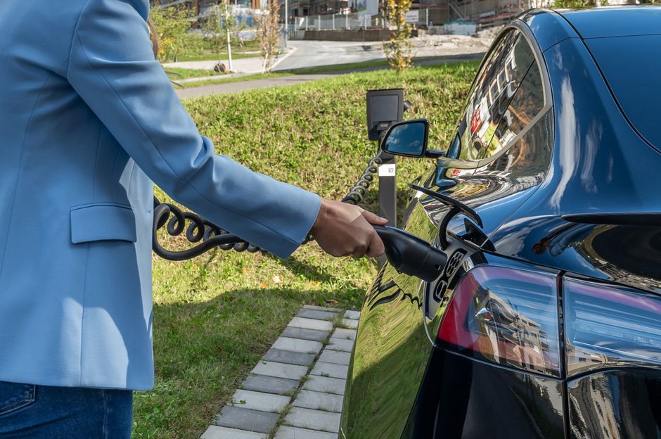 Persona conectando un coche eléctrico a una estación de carga al aire libre, mostrando la transición hacia la energía verde.