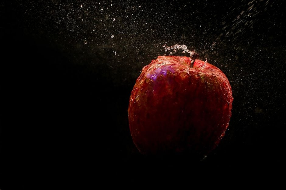 Un primer plano de una manzana roja con gotas de agua, contra un dramático fondo negro, capturada en movimiento.