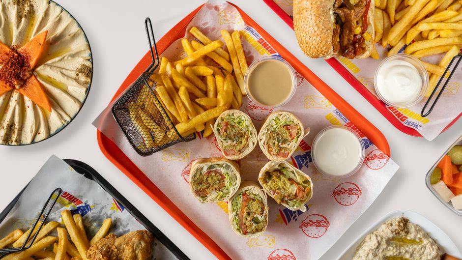 Vista cenital de diversos platos de comida rápida de Oriente Medio, como hummus, wraps de falafel, patatas fritas y salsas.