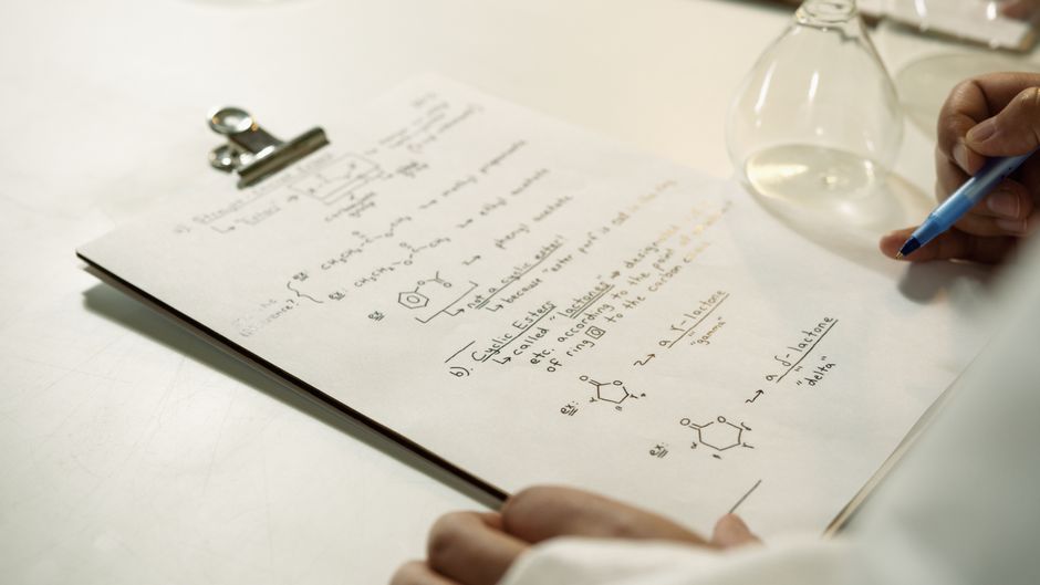 Una vista en primer plano de fórmulas químicas escritas a mano en un clipboard en un entorno de laboratorio.