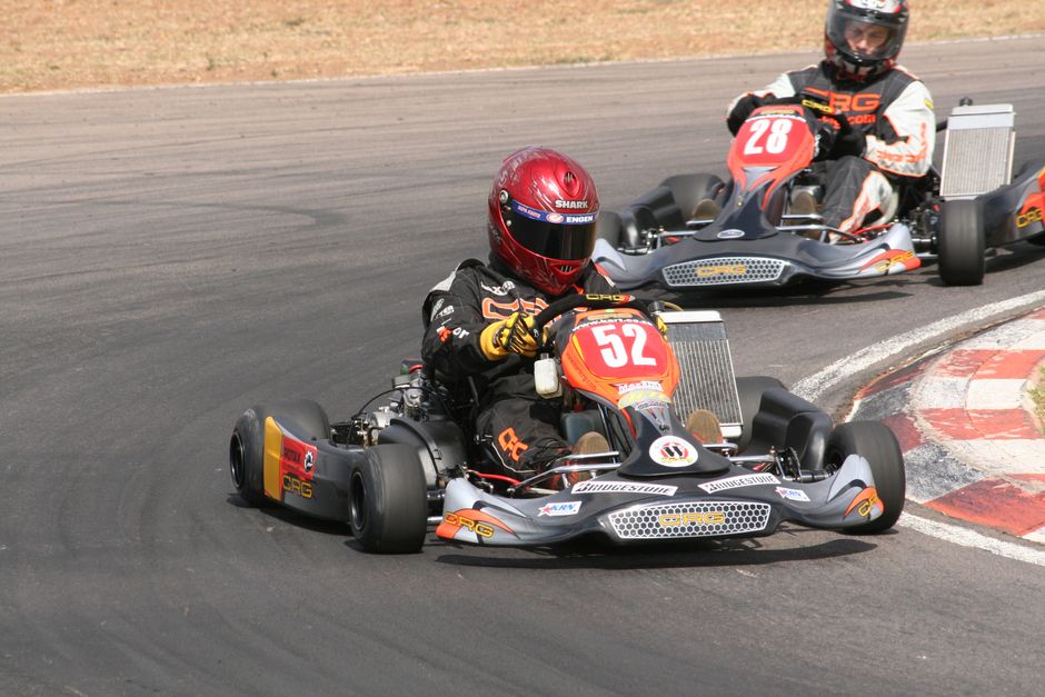 Intensa acción de carreras de karts con competidores en una pista curva y equipados, enfatizando la velocidad y el deporte.