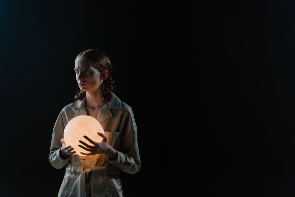 Una mujer sosteniendo una esfera iluminada en un entorno de estudio oscuro, evocando un sentido de misterio.