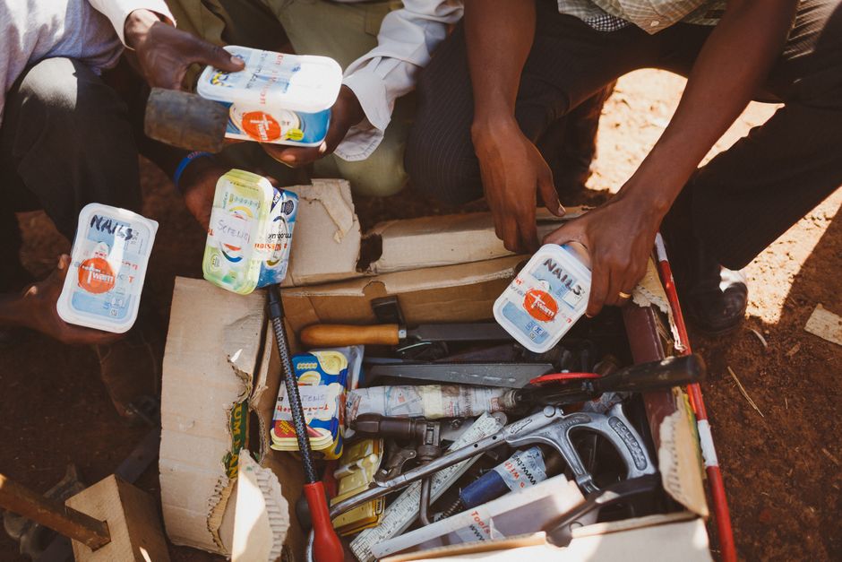 Personas organizando herramientas en una caja de cartón al aire libre en Wakiso, Uganda.