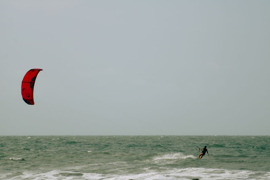 Un kitesurfista solitario se desliza sobre las olas del océano bajo un milano real en un día despejado.