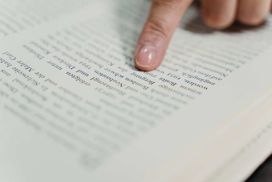Una vista detallada de un dedo apuntando al texto de un libro, enfatizando la lectura y el estudio.