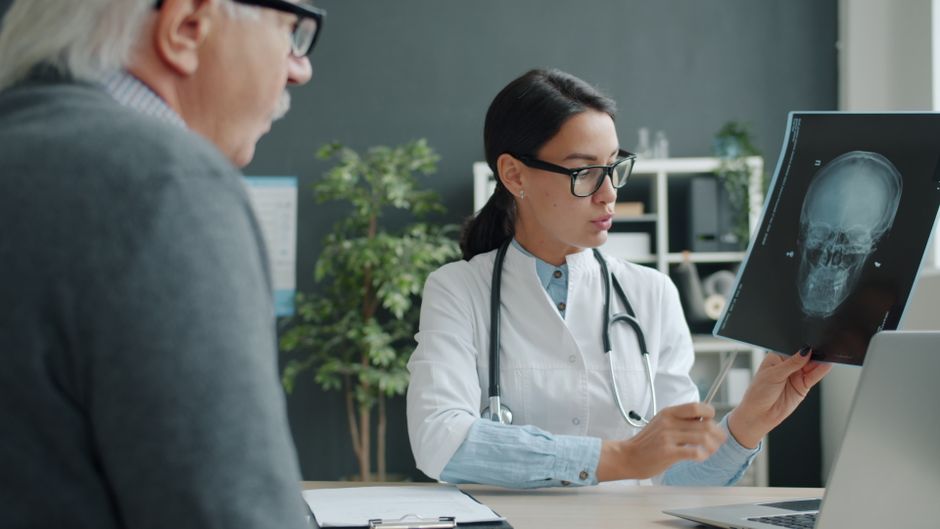 Una doctora conversa con un paciente anciano sobre una radiografía cerebral en un consultorio médico moderno.