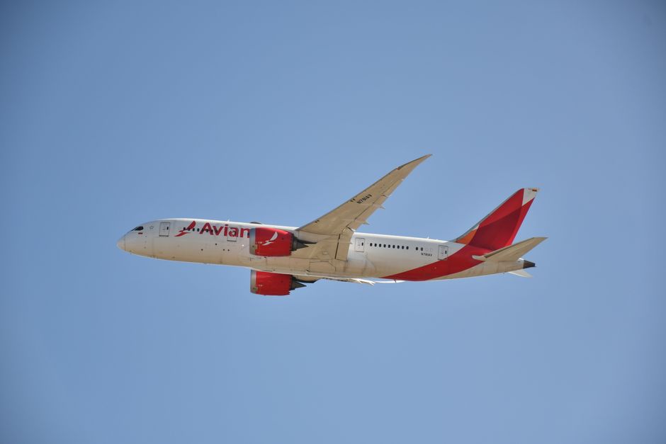 Un avión comercial de pasajeros volando contra un cielo azul claro, mostrando viajes y aviación.