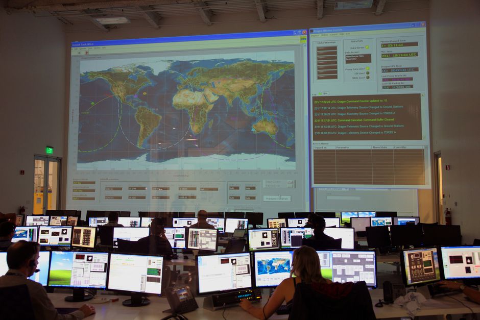 Sala de control con profesionales analizando datos globales en múltiples pantallas y un mapa mundial proyectado.