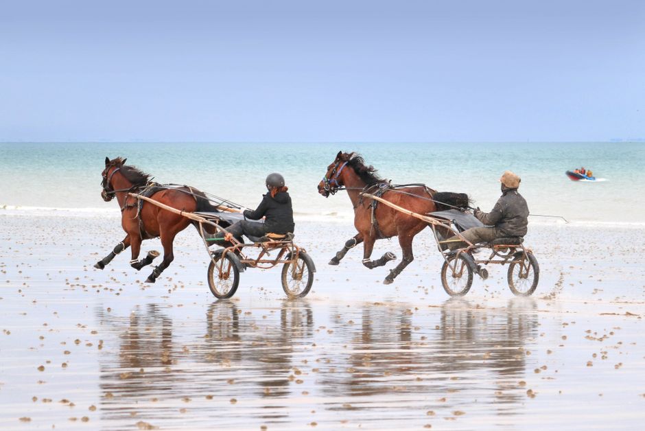 Dos carros de caballos compitiendo en las arenas húmedas de la playa de Jullouville, Normandía, Francia.