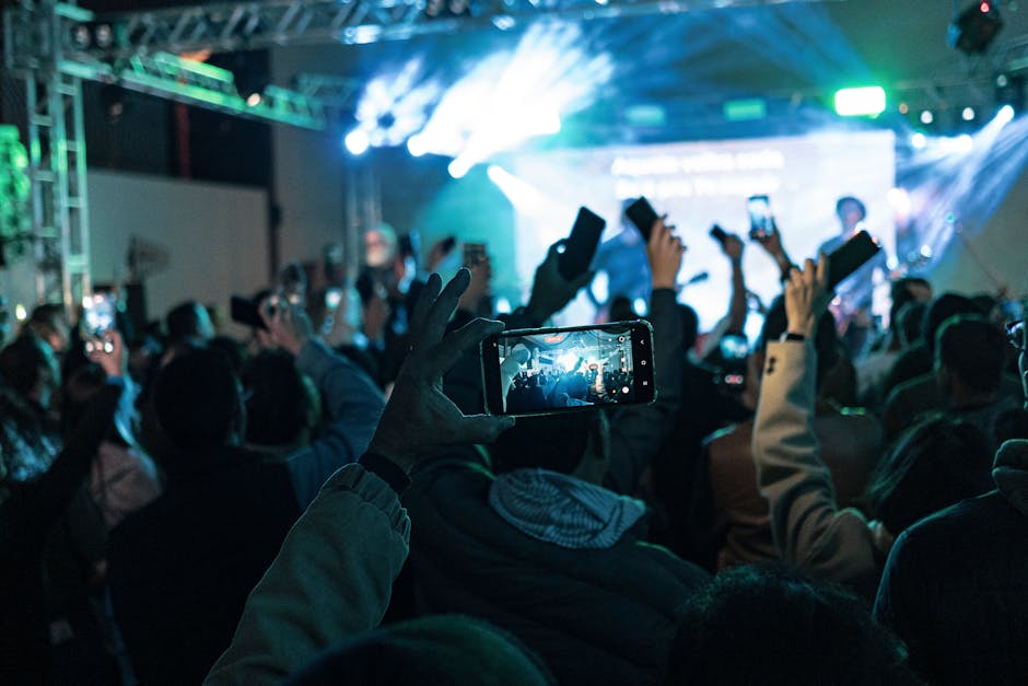 Una multitud animada captura los momentos del concierto en sus teléfonos inteligentes, las luces vibrantes crean una atmósfera dinámica.