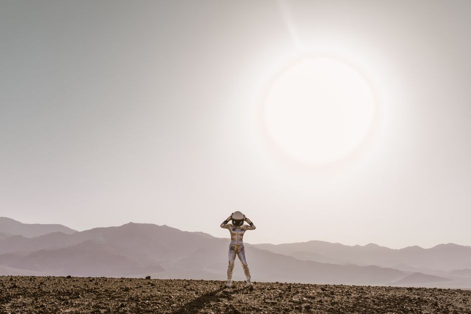 Astronauta en traje espacial de pie bajo un sol brillante en un paisaje desértico árido, evocando una atmósfera de ciencia ficción.