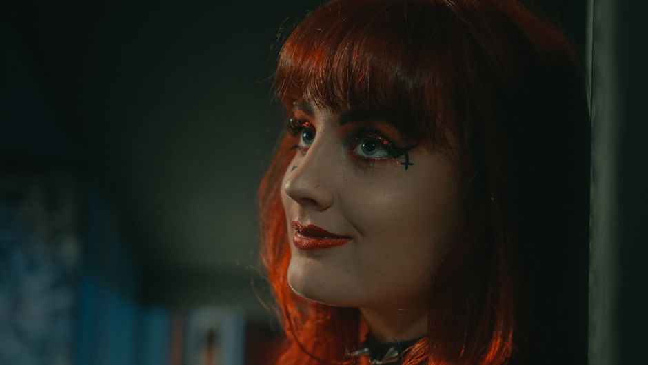 Retrato en primer plano de una mujer con cabello rojo intenso, maquillaje audaz y un diseño artístico de delineador.