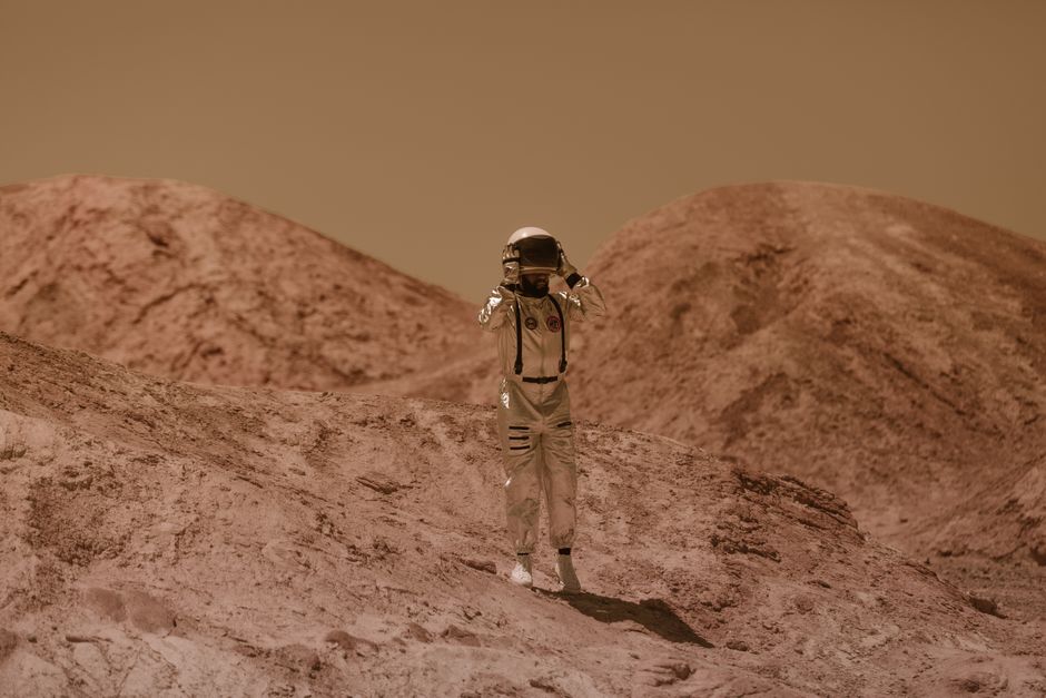 Astronauta en un traje espacial detallado explora un paisaje rocoso similar a Marte al aire libre, evocando una aventura de ciencia ficción.