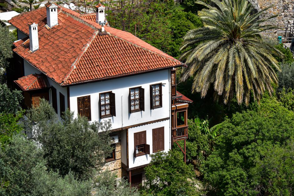 Encantadora casa mediterránea tradicional con techo de tejas rojas en medio de exuberante vegetación y palmera.