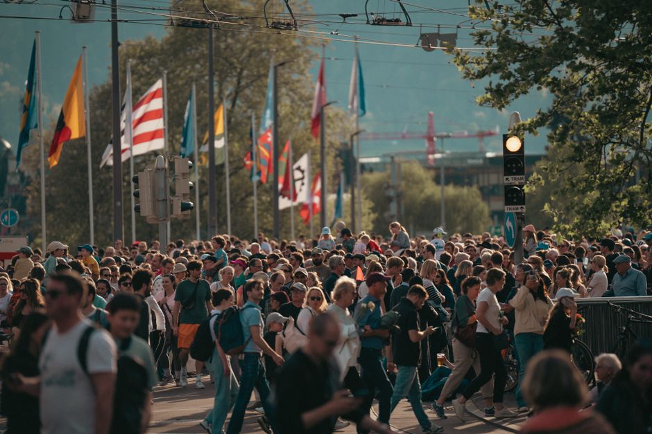 Una calle bulliciosa de la ciudad con una multitud diversa y banderas internacionales bajo un cielo soleado.
