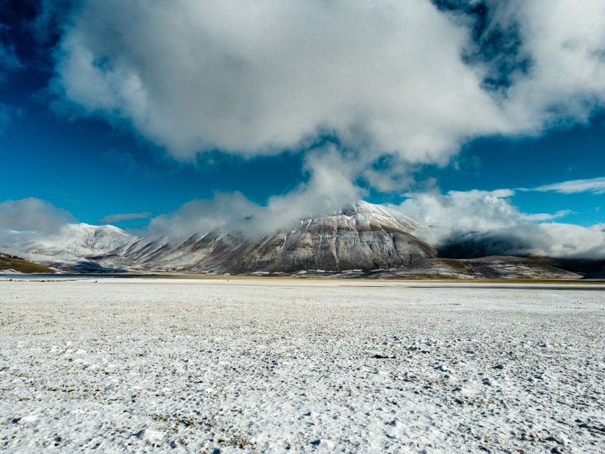 Majestuosas montañas cubiertas de nieve bajo un cielo azul con nubes esponjosas.
