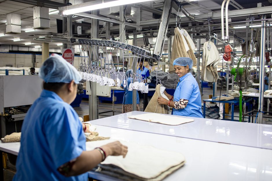 Trabajadores con uniformes azules procesan textiles en una moderna fábrica automatizada. Interior luminoso.