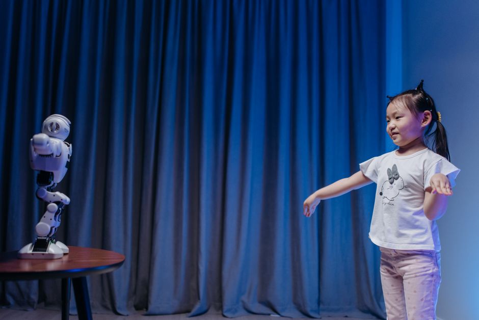 Una niña pequeña interactúa de manera juguetona con un robot humanoide en un entorno moderno interior.