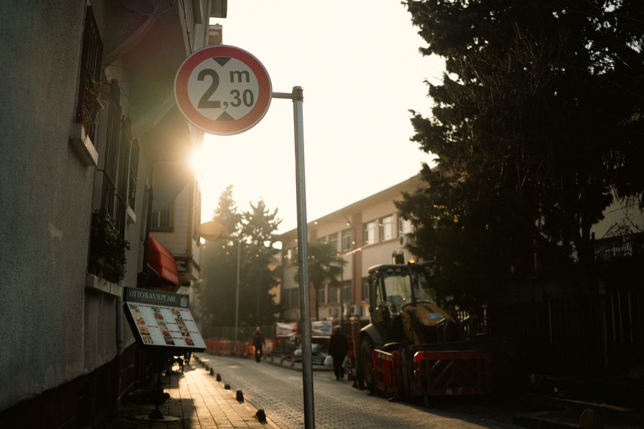 El atardecer ilumina una calle urbana con una señal de límite de altura de 2,3 metros y un vehículo de construcción.