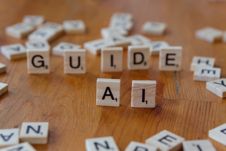 Letras de Scrabble que deletrean 'GUIDE' y 'AI' sobre una superficie de madera, lo que sugiere dirección y tecnología.