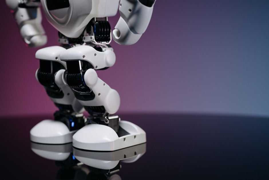 Una imagen detallada en primer plano de las piernas y pies de un robot moderno, reflejándose en una superficie brillante.