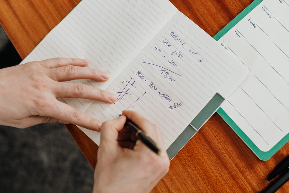 Una persona escribiendo cálculos en un cuaderno sobre un escritorio de madera.