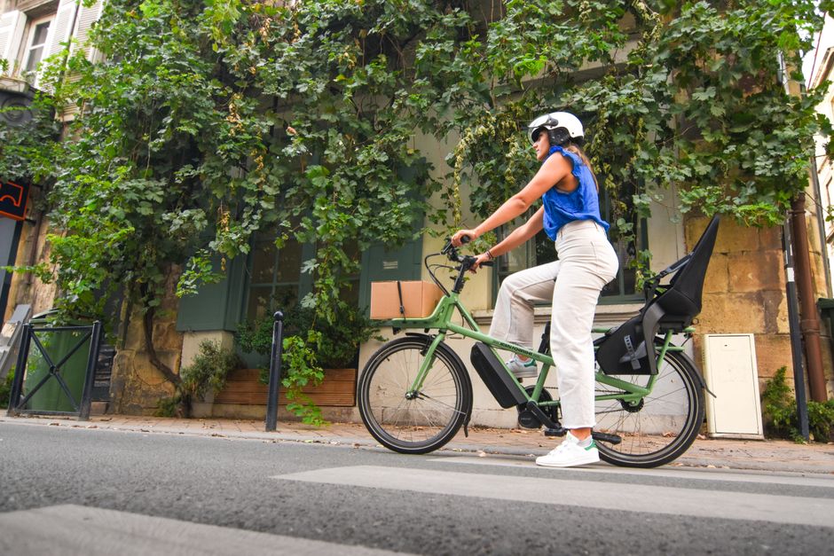 Mujer en una bicicleta eléctrica montando por una calle frondosa de París. Concepto de ciclismo urbano.