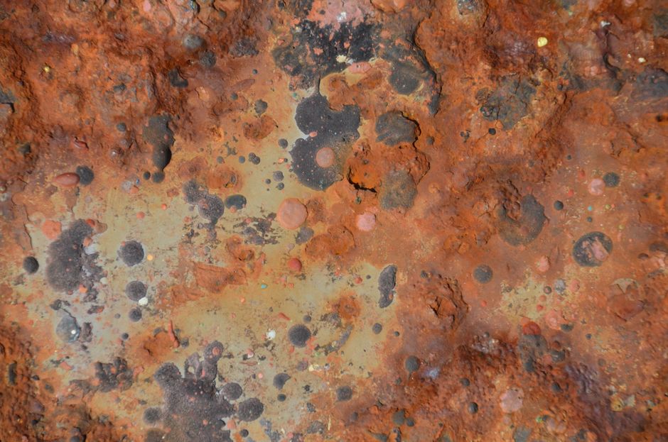 Acercamiento a una superficie metálica oxidada y corroída con un patrón intrincado de colores.