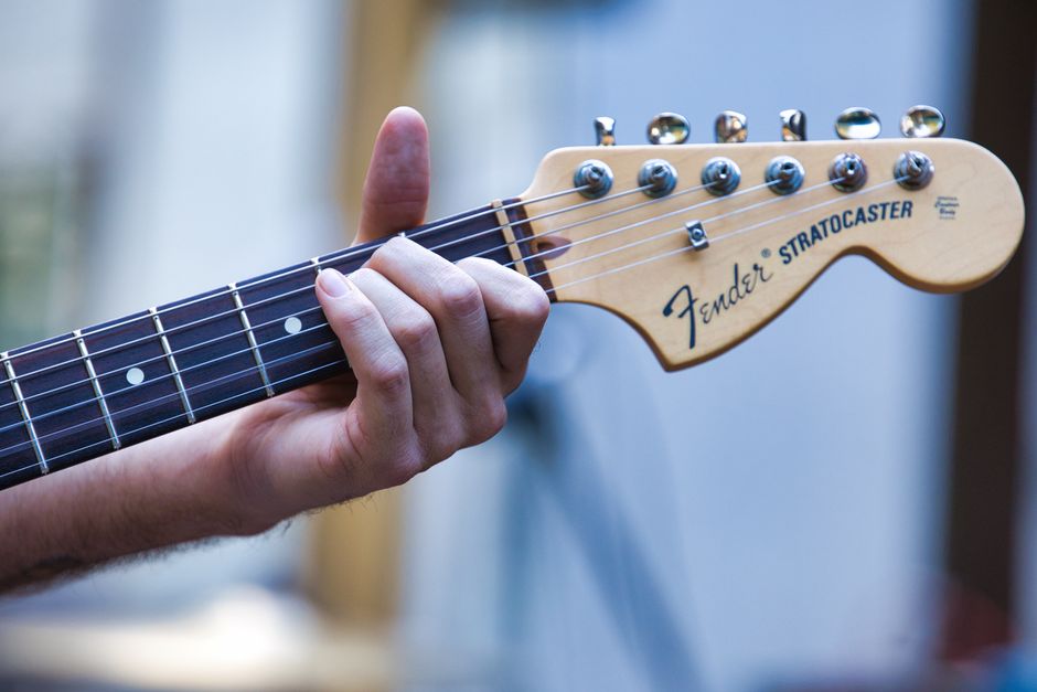 Vista en primer plano de la mano de un guitarrista tocando un Fender Stratocaster al aire libre.