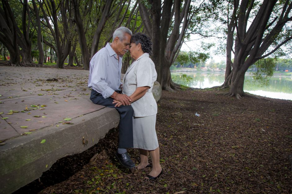 Una pareja de ancianos se abraza tiernamente bajo los árboles junto a un lago, mostrando amor y compañerismo.