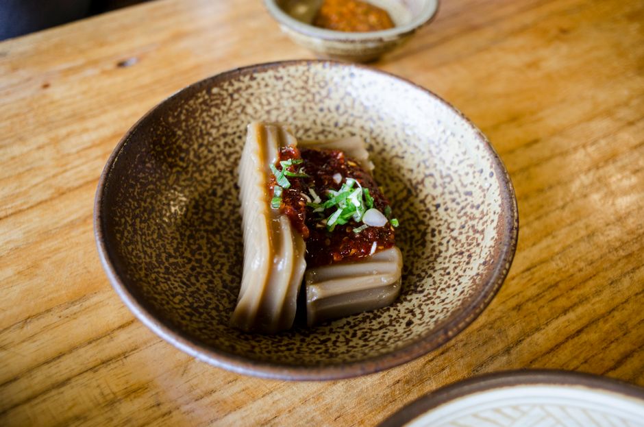 Un tazón rústico sobre una mesa de madera contiene un postre de gelatina asiática tradicional cubierto con salsa picante y cebollino.