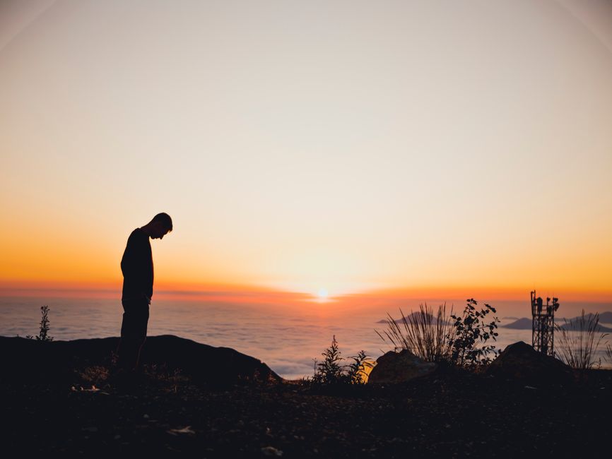 Una persona perfilada contra un vibrante atardecer en una montaña, capturando una vista serena.