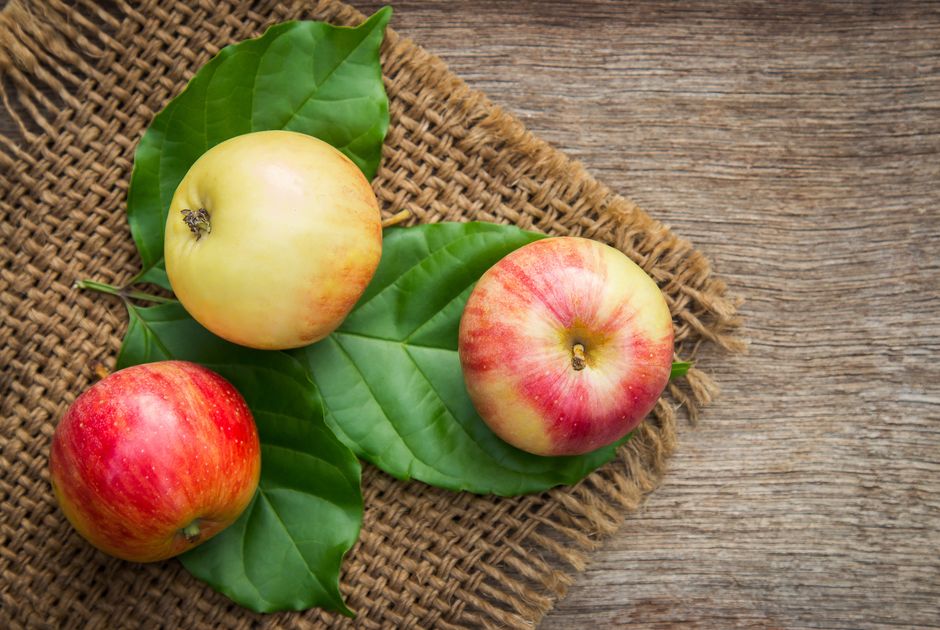 Tres manzanas maduras sobre hojas con un fondo rústico de madera, enfatizando frescura y nutrición.