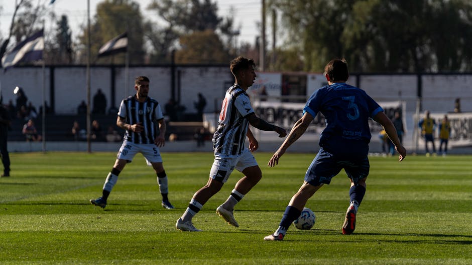 Los jugadores compiten en un dinámico partido de fútbol bajo un cielo despejado en un campo de césped.