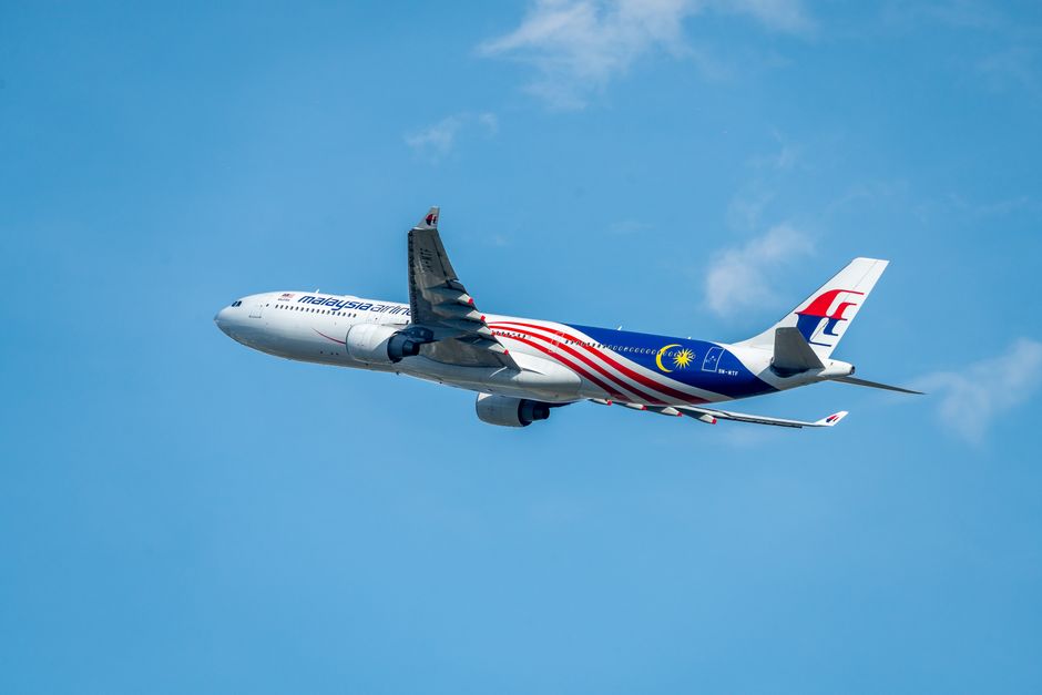 Un avión de Malaysia Airlines volando contra un cielo azul claro, mostrando su diseño.