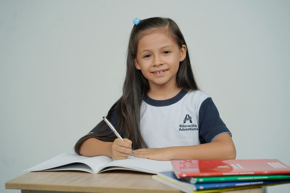 Una niña sentada en un escritorio, estudiando con libros abiertos y sonriendo.