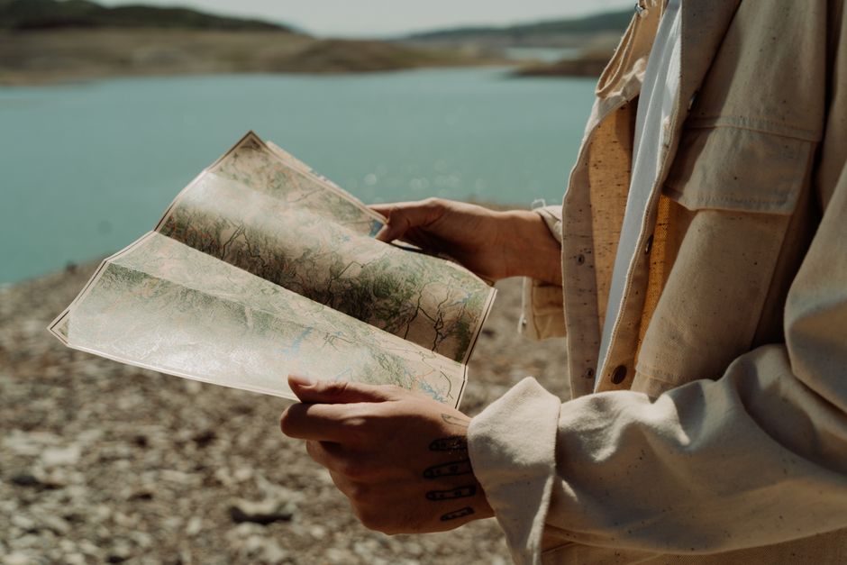 Persona sosteniendo un mapa cerca de un lago sereno, encarnando la exploración y la aventura.
