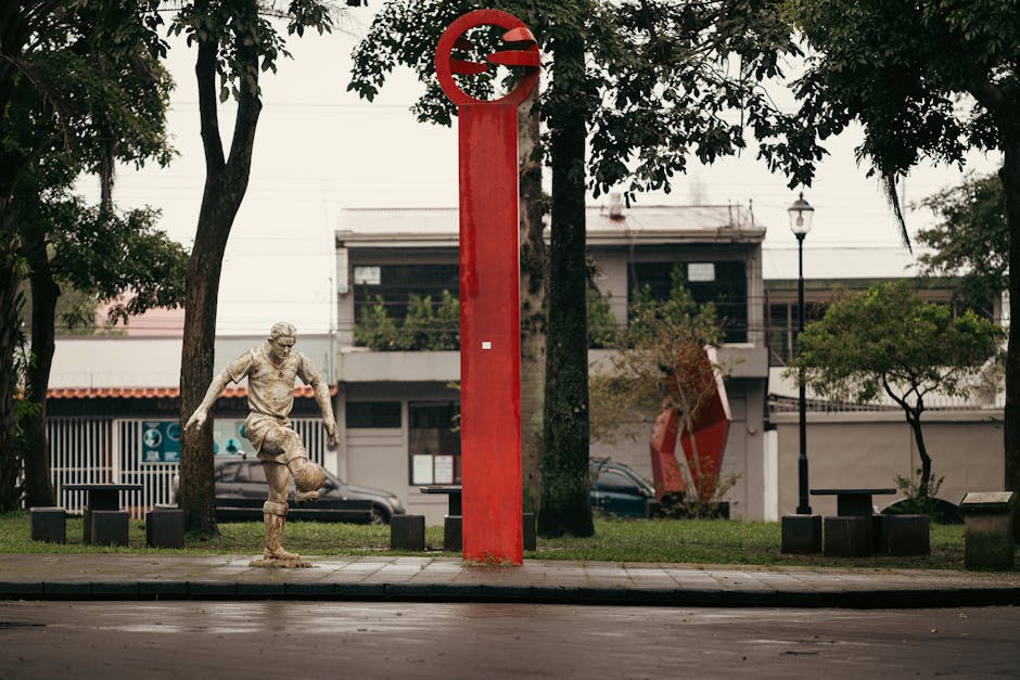 Una estatua de piedra de un jugador de fútbol junto a una columna roja en el parque de Alajuela, Costa Rica.