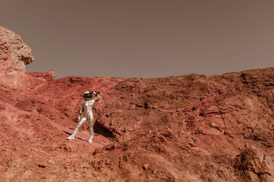Un astronauta con un traje espacial plateado examina un terreno marciano desolado, evocando la exploración de ciencia ficción.