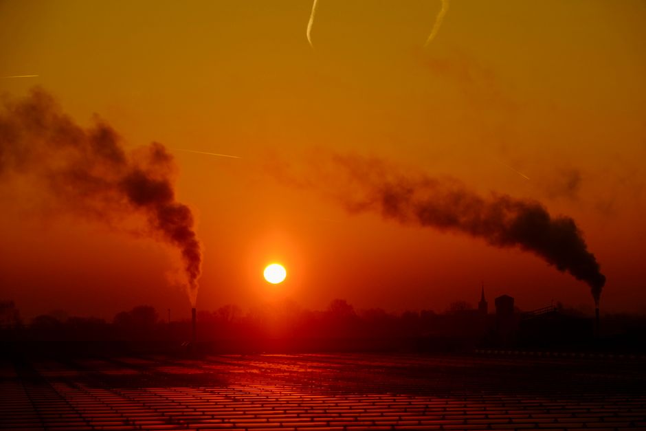 Puesta de sol sobre un paisaje industrial con emisiones de humo resaltando la contaminación del aire.