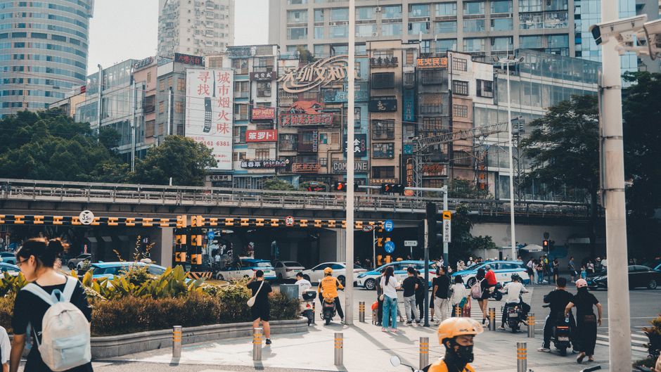 Intersección urbana animada con peatones y tráfico bajo edificios urbanos con señalización colorida.