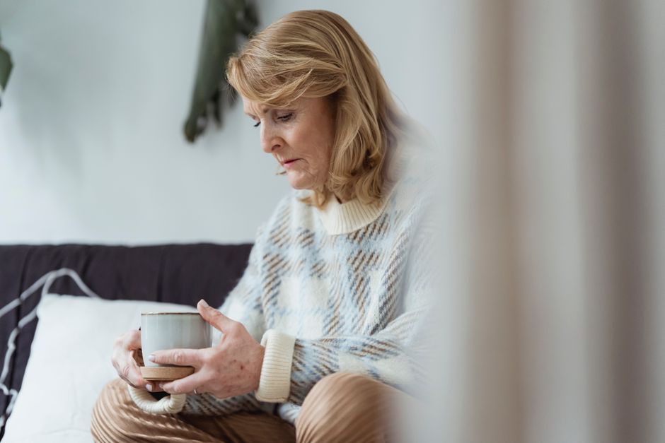 Mujer anciana sentada reflexiva con una taza de café, en interiores, ambiente relajado.