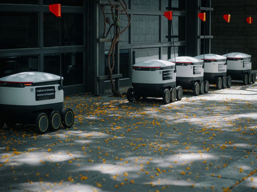 Robots de entrega autónomos alineados al aire libre, mostrando innovaciones en tecnología de transporte moderno.