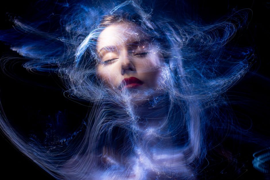 Retrato abstracto de una mujer con senderos de luz azul en espiral y ojos cerrados.