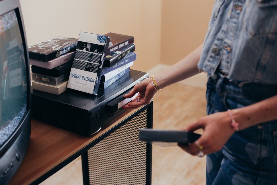 Una persona configurando un videograbador con cintas VHS en un acogedor entorno interior.