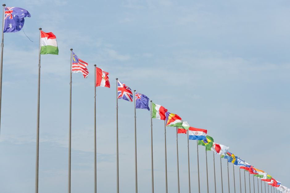 Una serie de banderas internacionales ondeando en fila contra un cielo azul claro, simbolizando la unidad global.