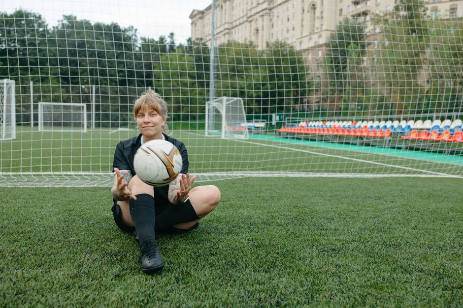 Una jugadora de fútbol sentada con un balón en un campo de fútbol, disfrutando de un descanso.